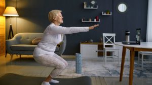 elderly woman squats while doing exercise in living room