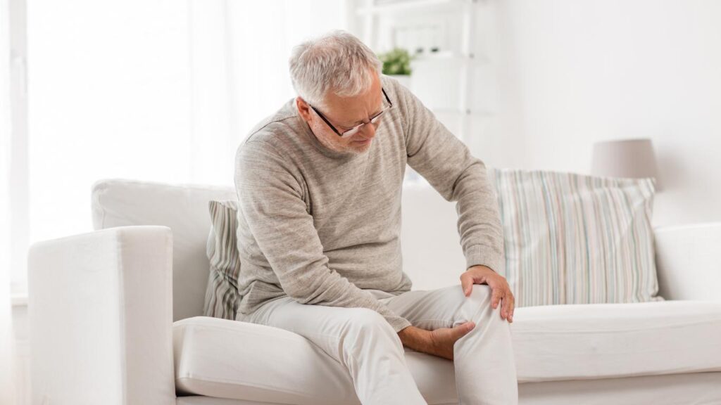 Older man grabs behind his knee and on top of it showing pain