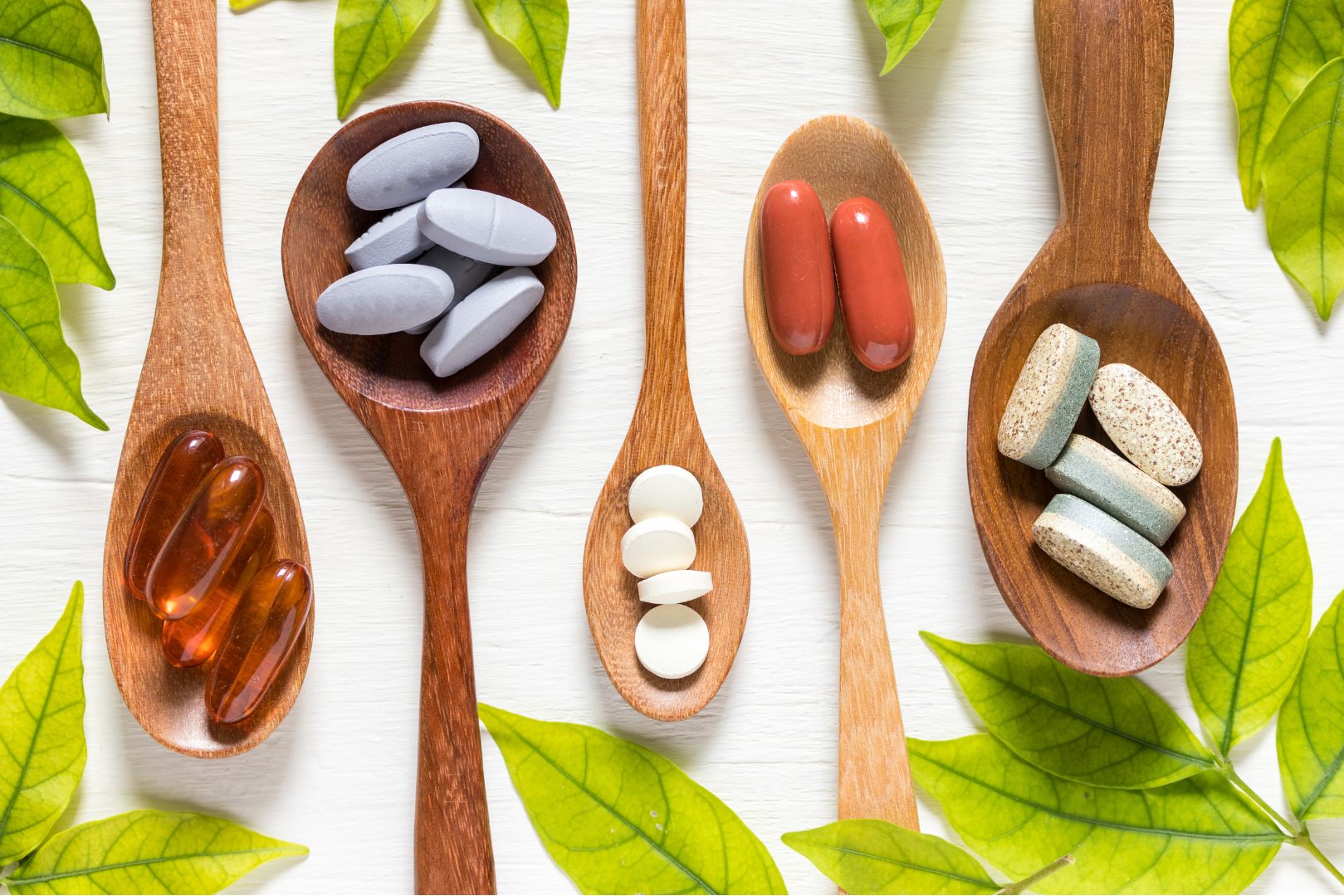 Vitamin D2 and D3 pills and capsules placed on wooden spoons with leaves in the background.