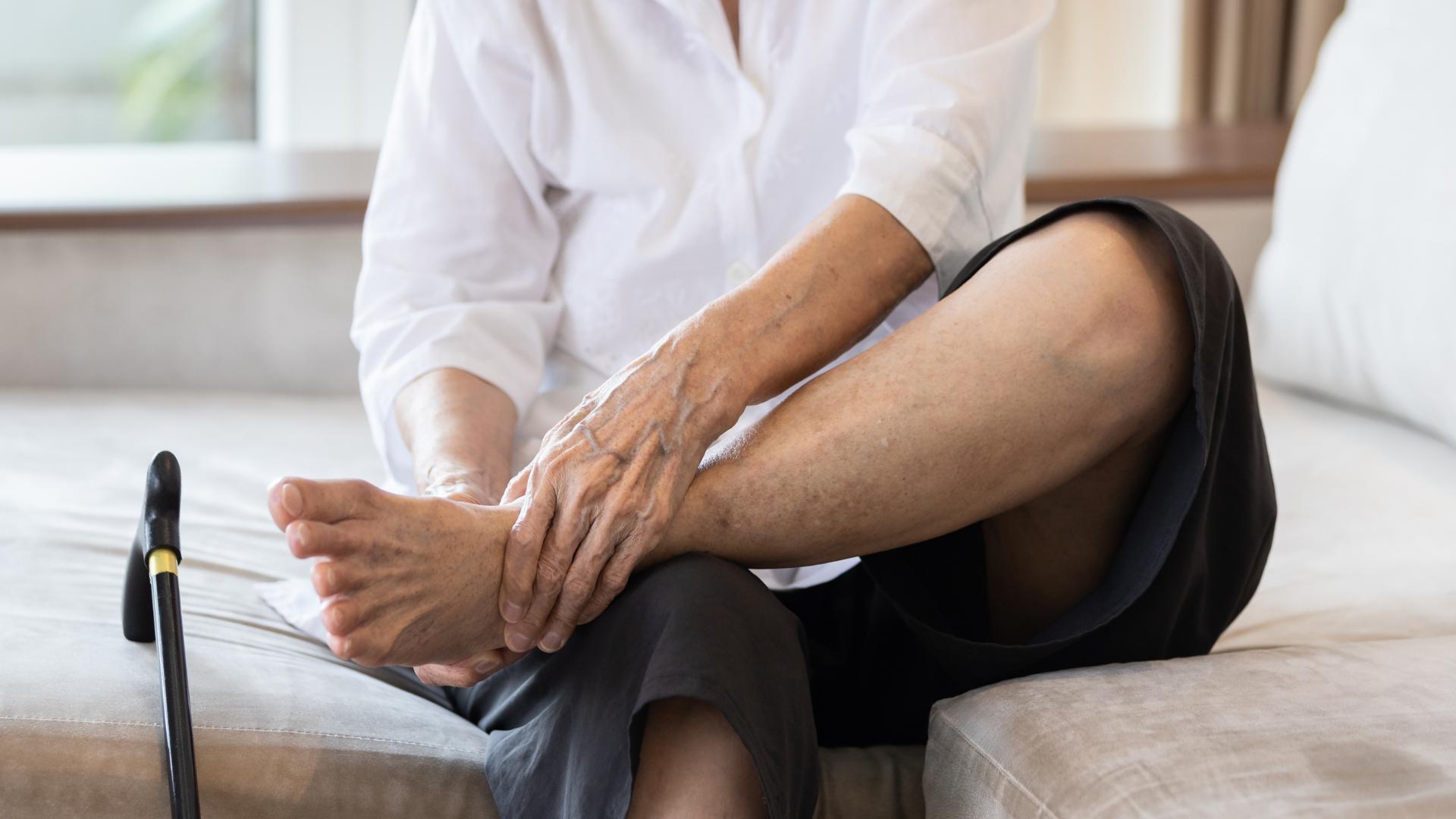 elderly woman sits on bed massaging foot due to pain