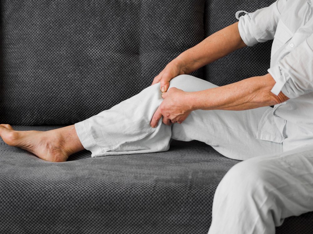 Text: Older adult massaging leg muscles to relieve stiffness and tension caused by a Baker’s cyst near the knee joint.