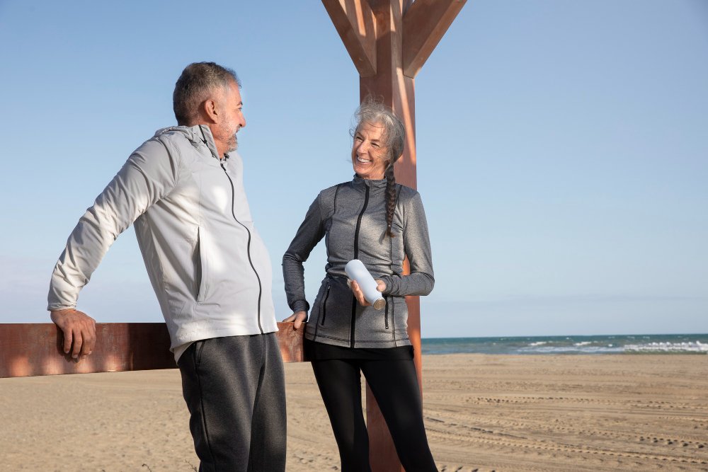 Senior couple stretching and smiling on the beach after a healthy knee exercise routine.
